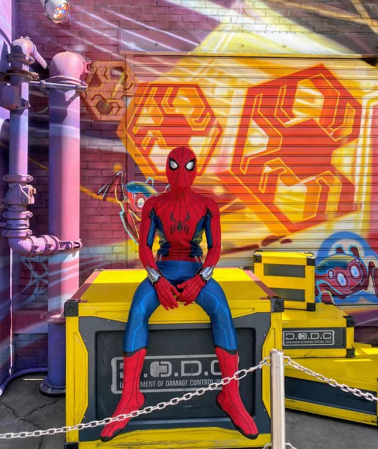 Spider-man sitting on a crate with a graffiti wall behind him. Movies to watch before going to Disneyland includes Spider-Man Far From Home. 