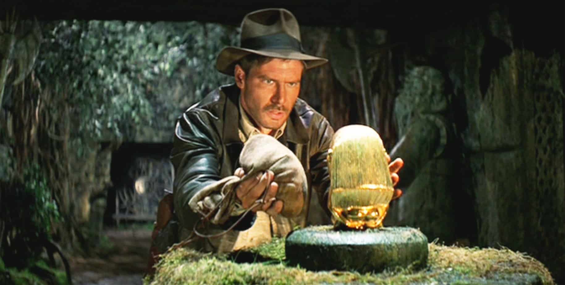 indiana-jones-movies-in -order. raiders-of-the-lost-ark. Man and a gold statue in a cave.